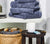 pile of towels, white container scented candle and towel in a basket