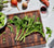 End-Grain hand crafted, black walnut, rectangular cutting board with vegetables on and surrounding it, with a white background.