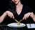 Woman dressed in black with black background cutting a gold strawberry with Brushed Gold Flatware on white Plates.